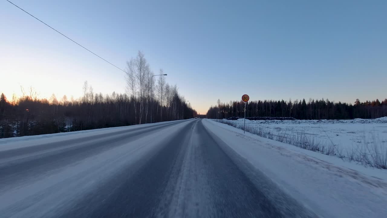Driving fast along a snowy road flanked by trees during a beautiful winter's morning in Finland