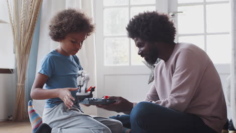 Black-middle-aged-father-and-son-sitting-on-the-floor-working-together-to-assemble-a-mechanical-kit-toy,-close-up,-side-view