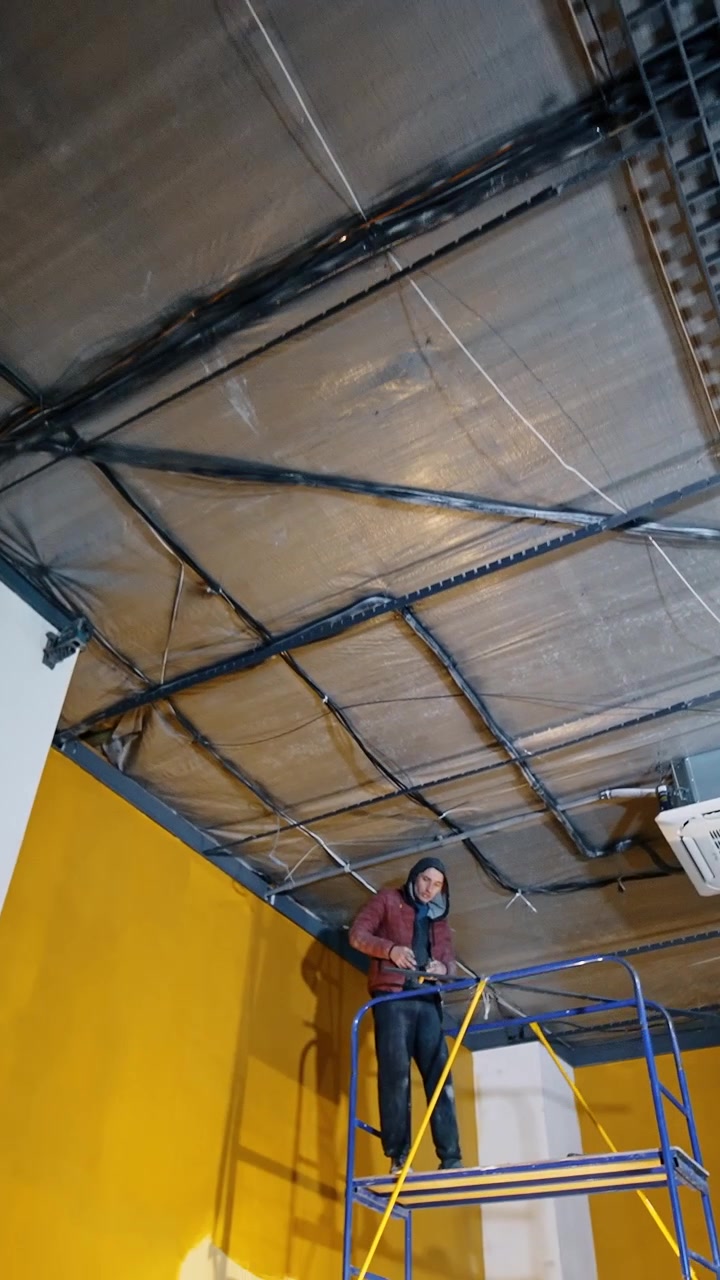 Ampia stanza con pareti gialle e colonne bianche. Uomini lavorano nella stanza riparando e installando l'illuminazione sul soffitto. Vista dal basso. Video verticale.