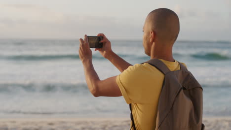 joven hispano usando un teléfono inteligente tomando fotos de la hermosa orilla del océano en la playa disfrutando de la vista panorámica del atardecer compartiendo la experiencia de las vacaciones