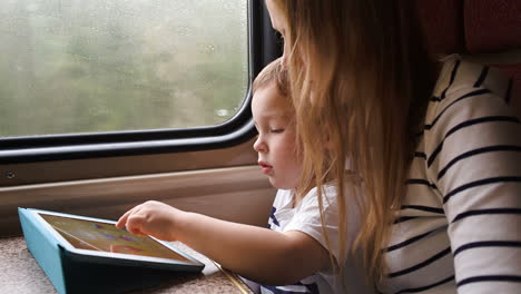 mother watching her son playing game on pad in the train