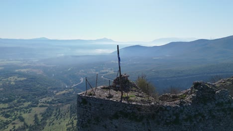 Asta-De-Bandera-Con-Bandera-Enrollada-Ondeando-Ligeramente-En-El-Viento-En-El-Borde-Del-Castillo-De-Karytaina-En-El-Peloponeso,-Grecia,-Retroceso-Aéreo-Al-Pueblo