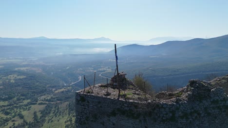 mástil de bandera con bandera rodada soplando ligeramente en el viento en el borde del castillo de karytaina en el peloponeso grecia, retirada aérea a la aldea
