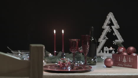 man takes a red glass from a decorated christmas table in a dark room with a chair in the foreground