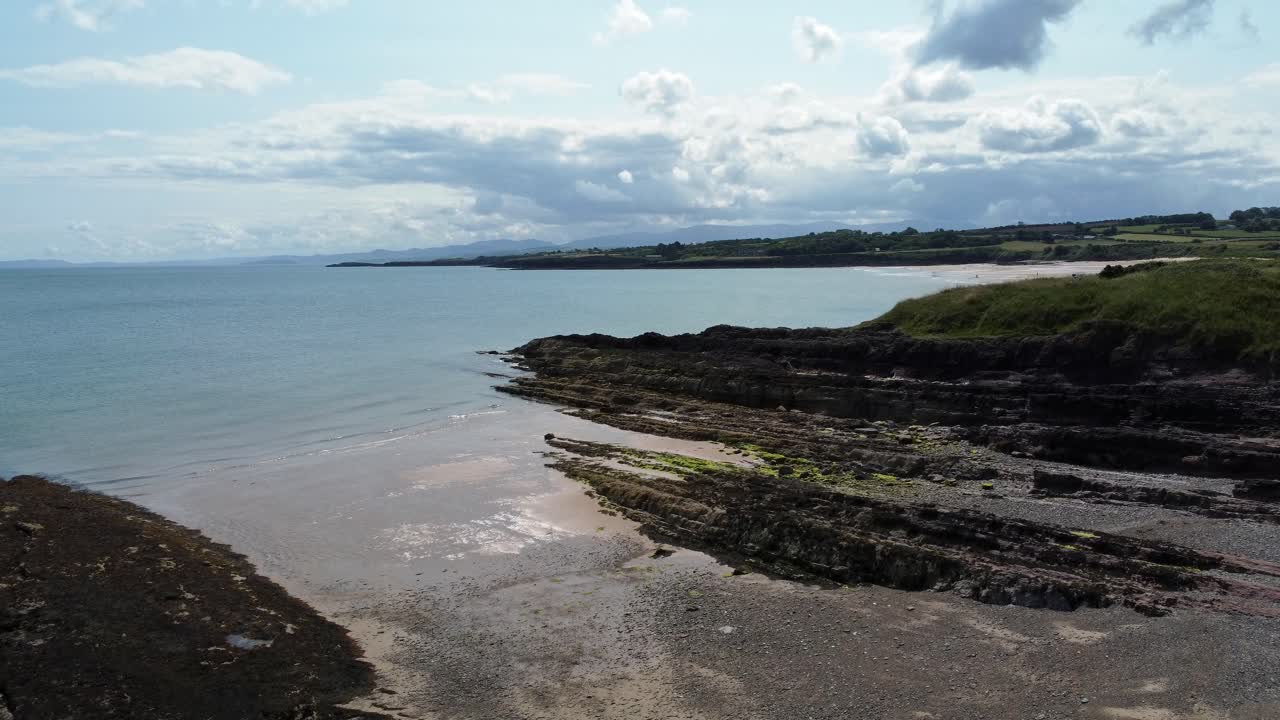 Traeth Lligwy idyllic rocky coast shoreline aerial view green pasture on rocky cliffs edge, rising forwards shot