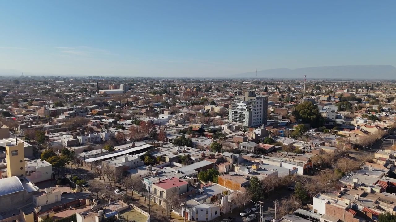 Gliding over residential streets and neighborhood houses in San Juan under clear, bright morning skies in Argentina.