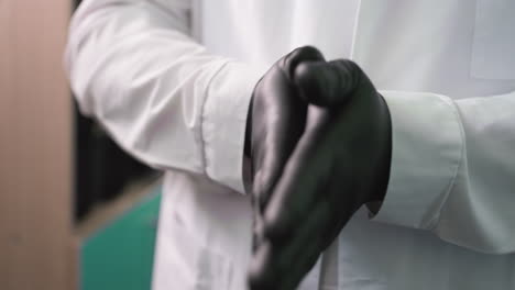 una vista de cerca de un hombre con guantes negros frotando sus manos juntos continuamente, con una vista de un estante de color marrón detrás