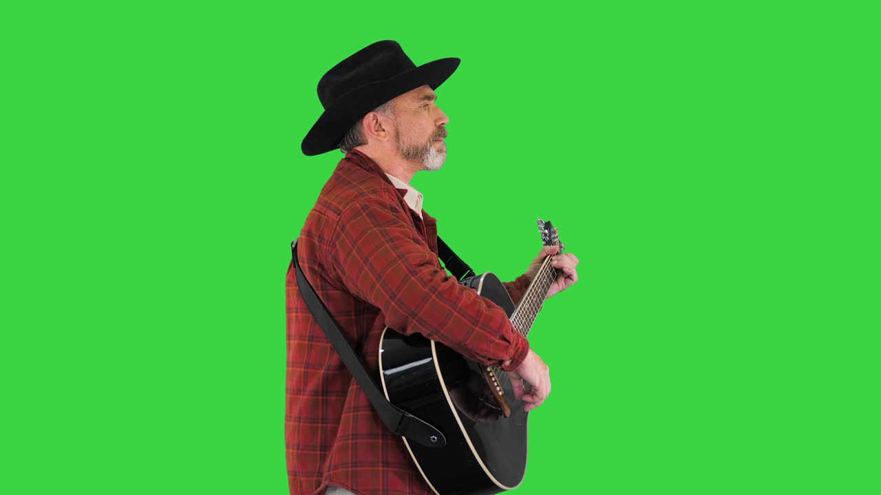 Uomo con cappello da cowboy che canta e suona la chitarra mentre cammina su uno schermo verde, Chroma Key.
