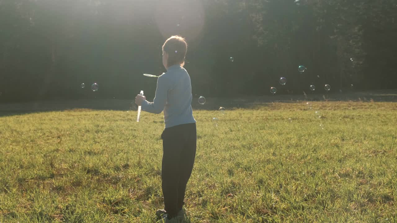 소년은 풀에서 비누 거품을 만들고 따뜻한 봄날에 놀고 있습니다.