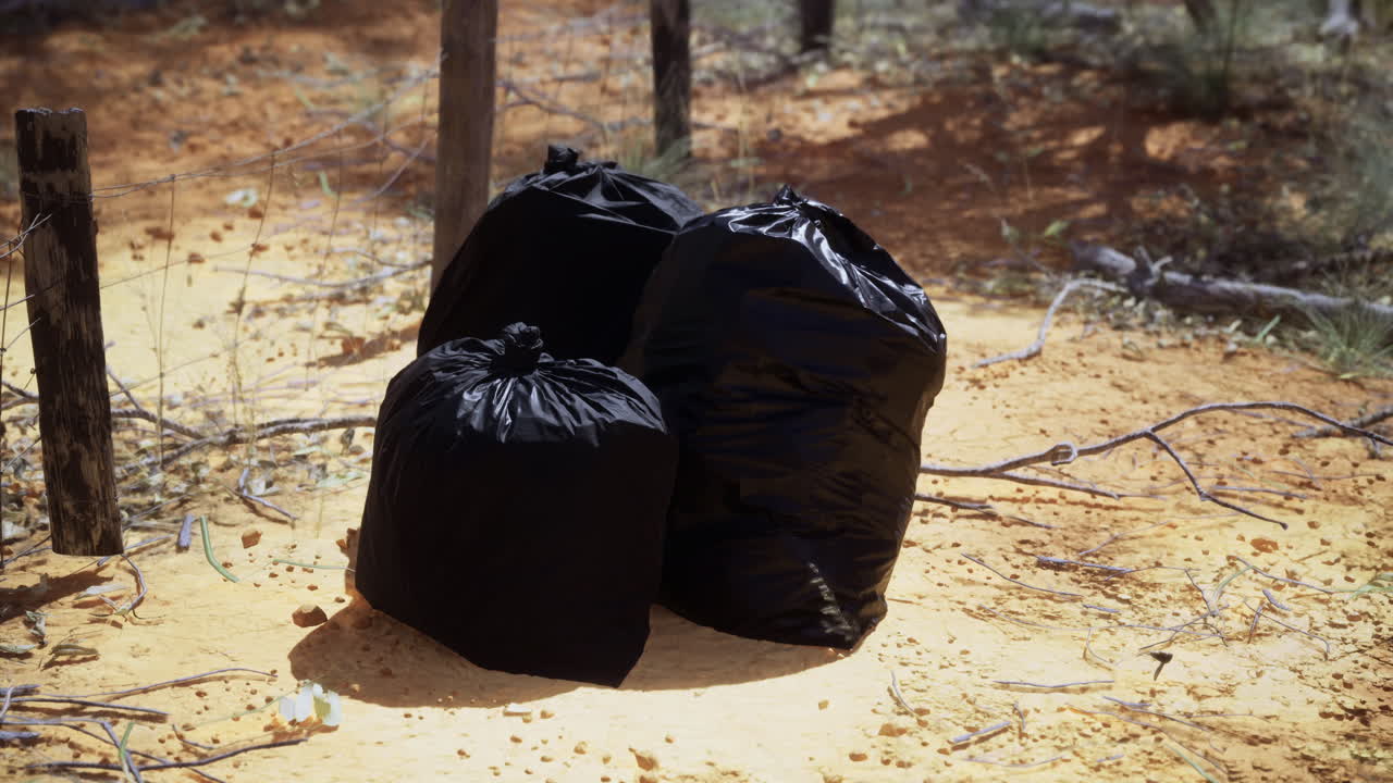 Bags of waste sit abandoned on the dry land under the scorching sun