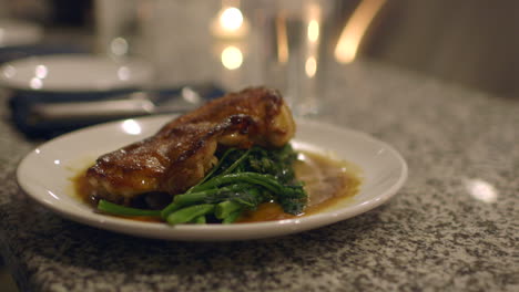 roast chicken and rapini plated on a counter at an upscale restaurant is sliced by customer