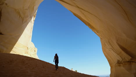 Silhouette-of-Woman-in-Great-Chamber,-Kanab,-Utah-USA-Walking-on-Sand-Under-Sandstone-Cove