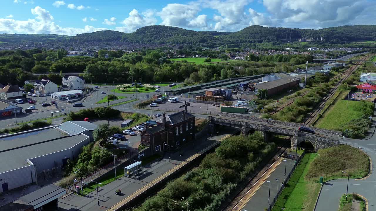 Aerial view circling above Abergele Welsh town train station and lush A55 mountain landscape
