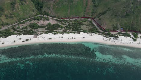 vista aérea de una playa de arena blanca con aguas claras de color turquesa y una ladera verde exuberante