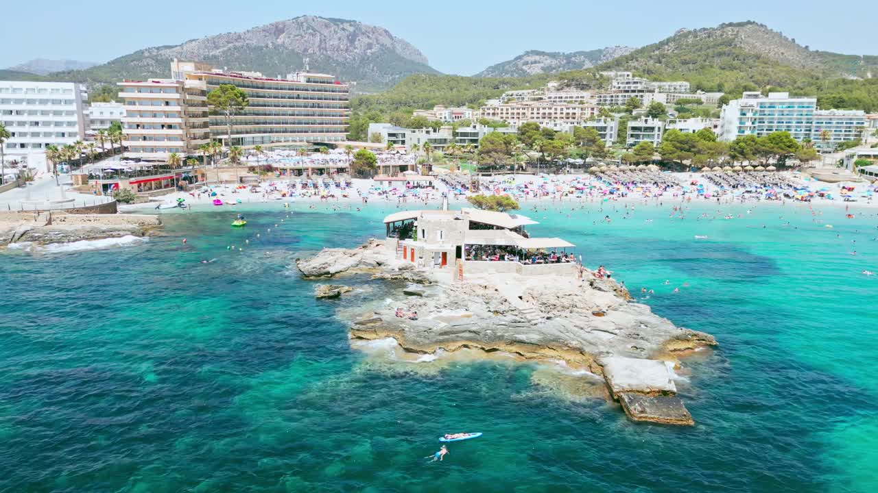 Aerial View of a Crowded Beach with a Restaurant on a Rock in Mallorca, Spain