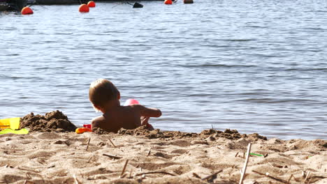 Kleiner-Blonder-Junge-Spielt-An-Heißen-Tagen-Am-Sonnenstrand-Im-Sand-An-Der-Wasserlinie