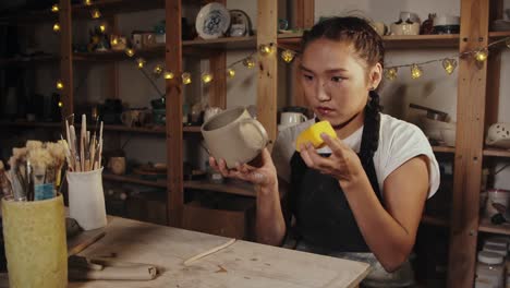 young woman potter smoothing out the clay cup using a sponge