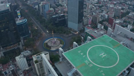 cámara de dron volando sobre un alto edificio de oficinas con helipuerto verde en la parte superior. vista aérea de la ciudad cerca del monumento del ángel de la independencia. ciudad de méxico, méxico