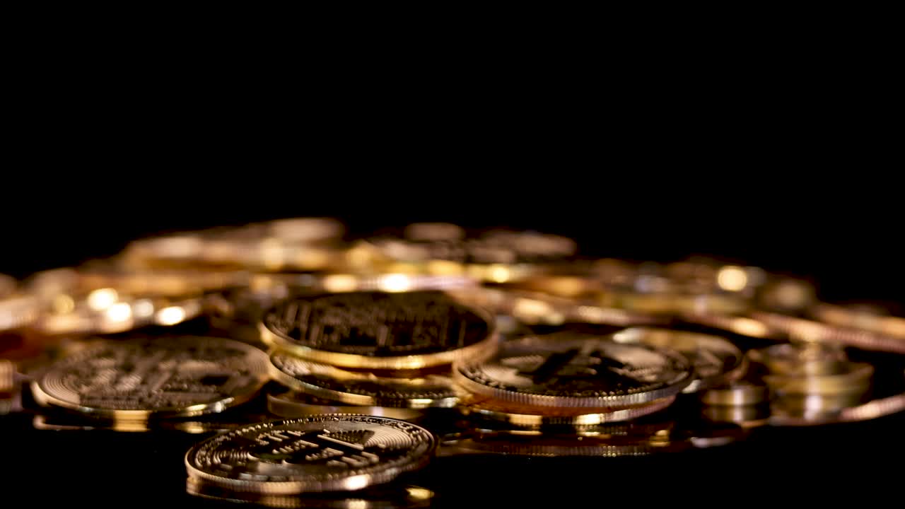 Gold coin with cryptocurrency symbol spins and settles among similar coins, dramatic low-key lighting