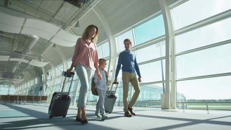 Padres-Con-Un-Hijo-Pequeño-Y-Agradable-Y-Maletas-Grandes-Sobre-Ruedas-Que-Pasan-Por-La-Cámara-En-El-Pasaje-Del-Aeropuerto-Mientras-Van-A-Las-Puertas-De-Salida-O-Llegada