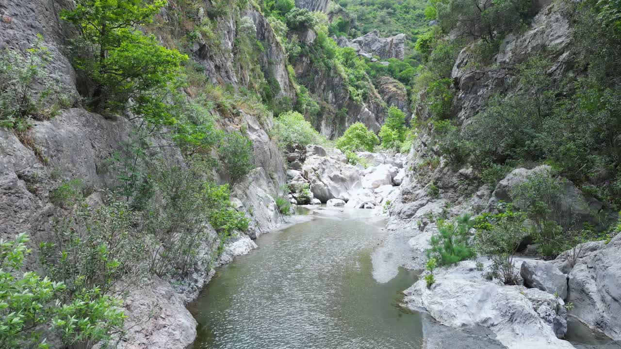 Aerial drone footage of Gole Ranciara, Sicily: rocky canyon with turquoise river, lush vegetation, and dramatic cliffs. Perfect for nature, adventure, and travel documentary projects