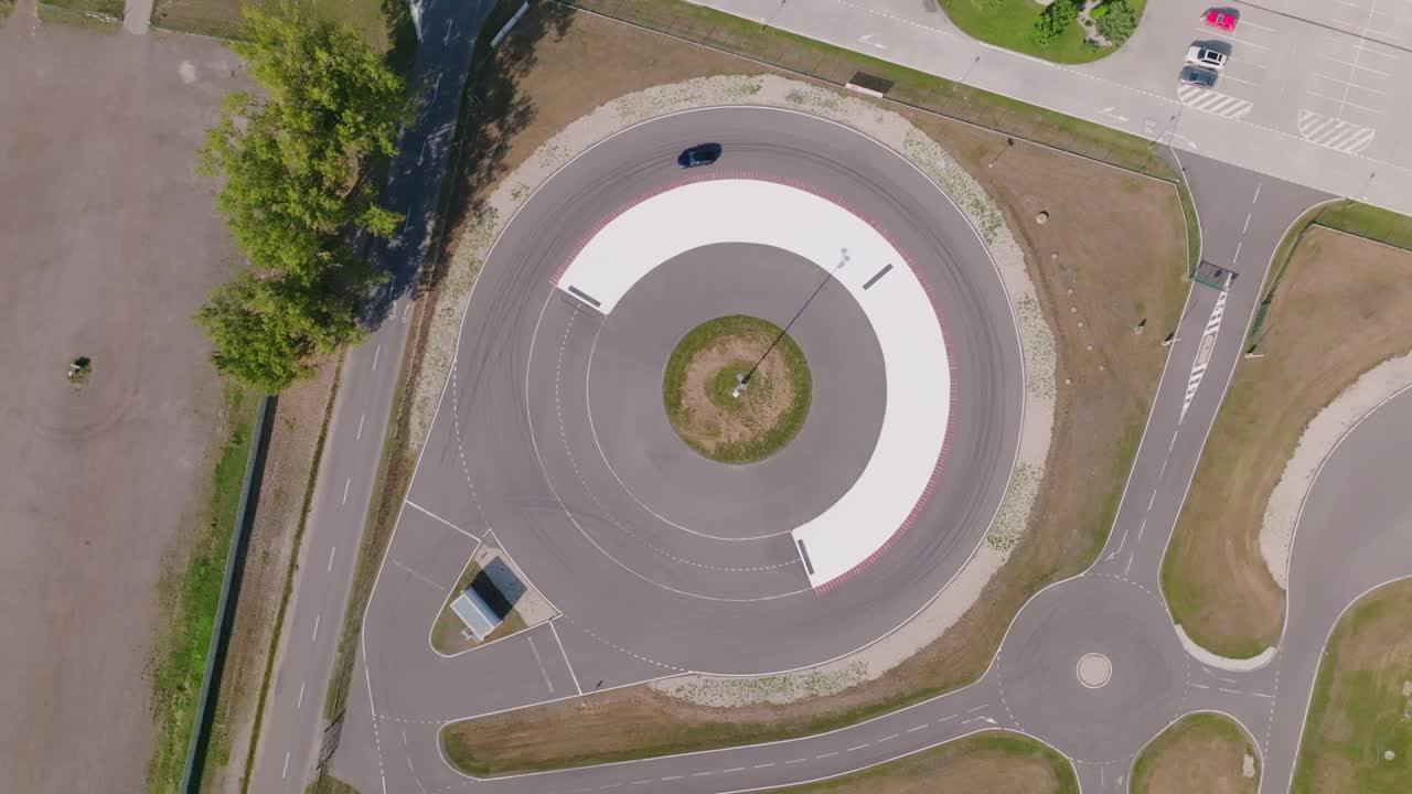 Drone aerial shot from directly above capturing a single car driving around a circular roundabout. Clean geometric road design with smooth traffic movement and urban infrastructure