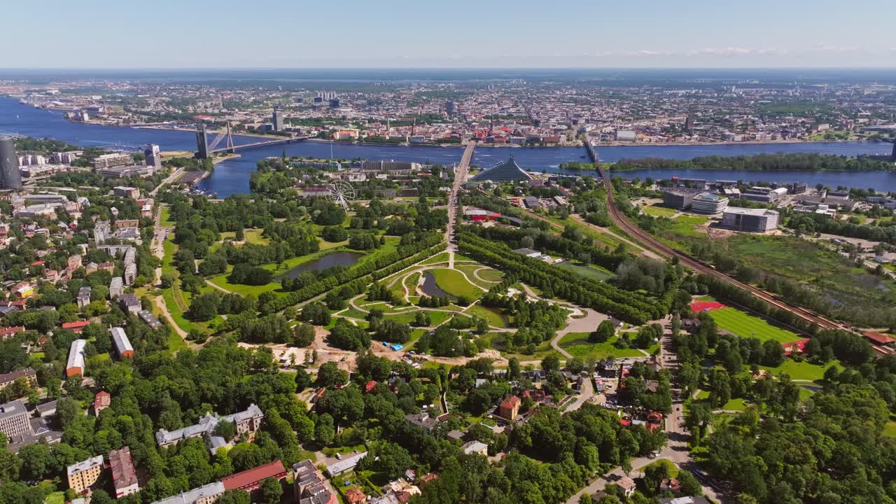 Summertime aerial pullback shows vibrant park merging with urban landscape, Riga