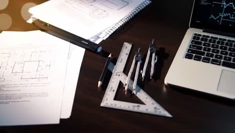a focused workspace: an engineer's desk featuring technical drawings, drafting tools, and a laptop screen displaying data analysis and graphs