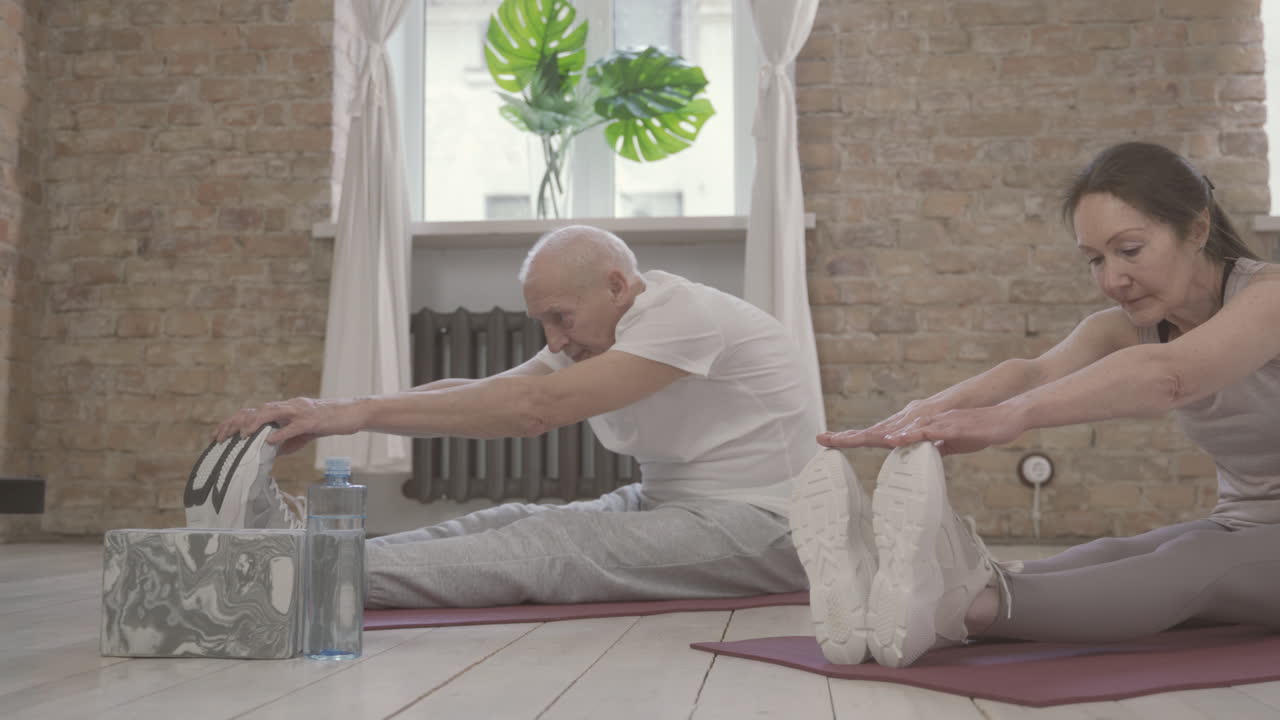 Old Female And Male Stretching And Exercising On Yoga Mat At Home