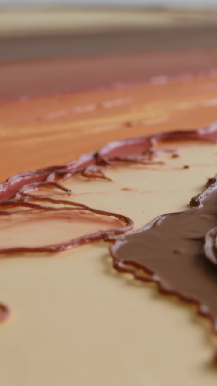 Video verticale: Telecamera in panoramica che rivela la crema che si unisce alla ganache su un tagliere di legno, mostrando anelli di caramello.