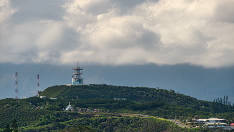 Tiro-De-Lapso-De-Tiempo-De-Nubes-Rodando-Sobre-Una-Torre-De-Radio-En-Una-Colina-Verde,-En-Noumea