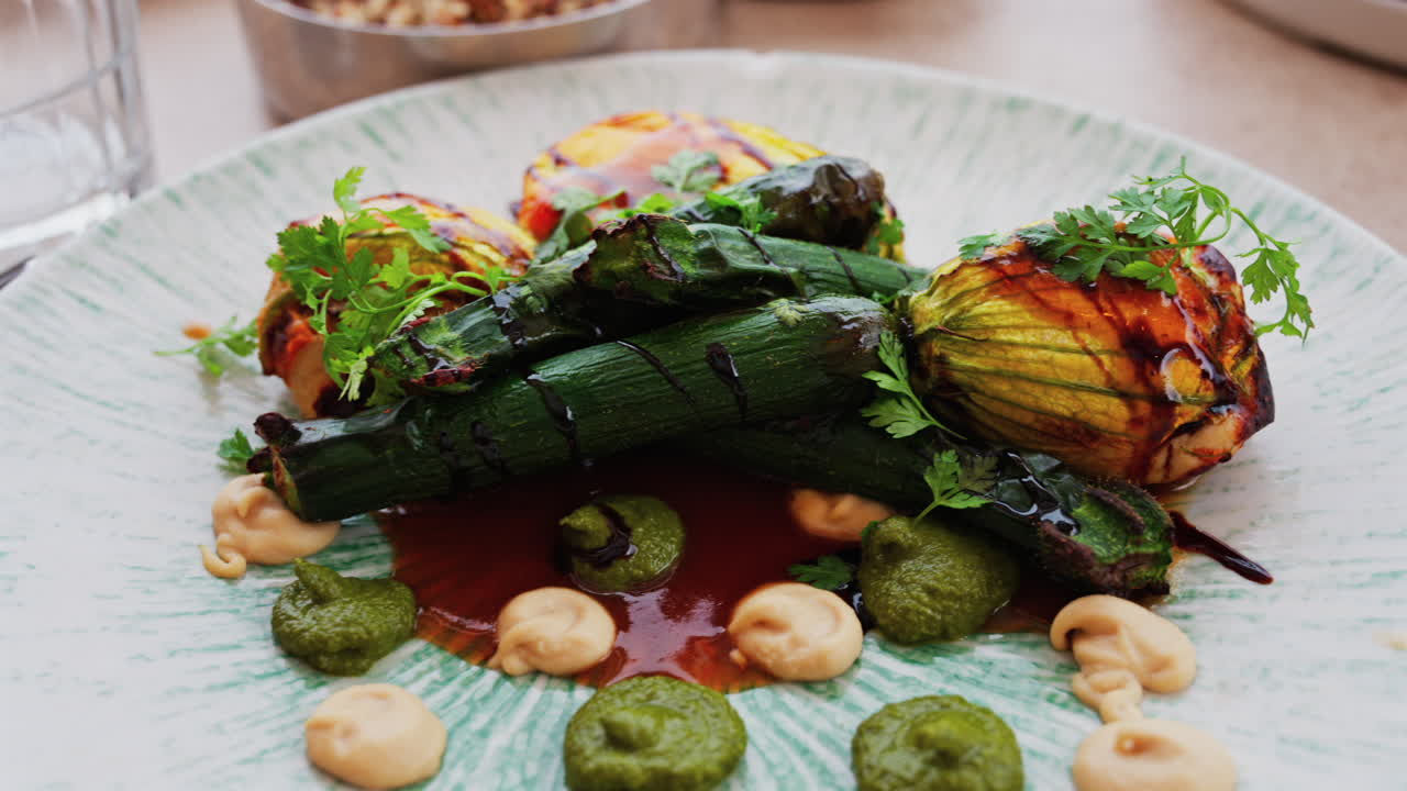 Close up of stuffed zucchini flowers with whole, grilled baby zucchinis on a white plate
