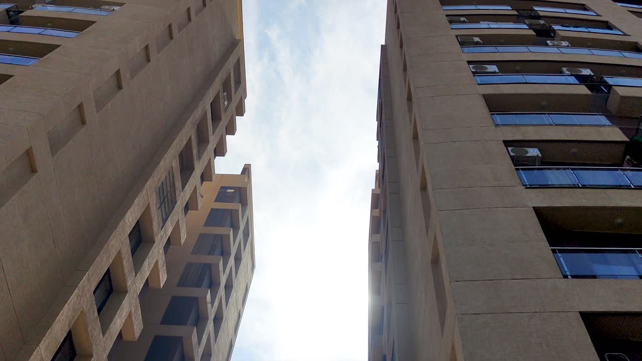 Stock footage of modern high-rise residential and commercial buildings from low-angle perspective, with sunlight and blue sky. Ideal for real estate, urban development, architecture, cityscape themes.