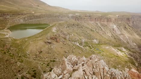 Beautiful-clear-calm-lake-near-pillar-rock-columns-on-the-green-hills-in-wild-mountain-upper-a-little-relax-lake-in-Iran