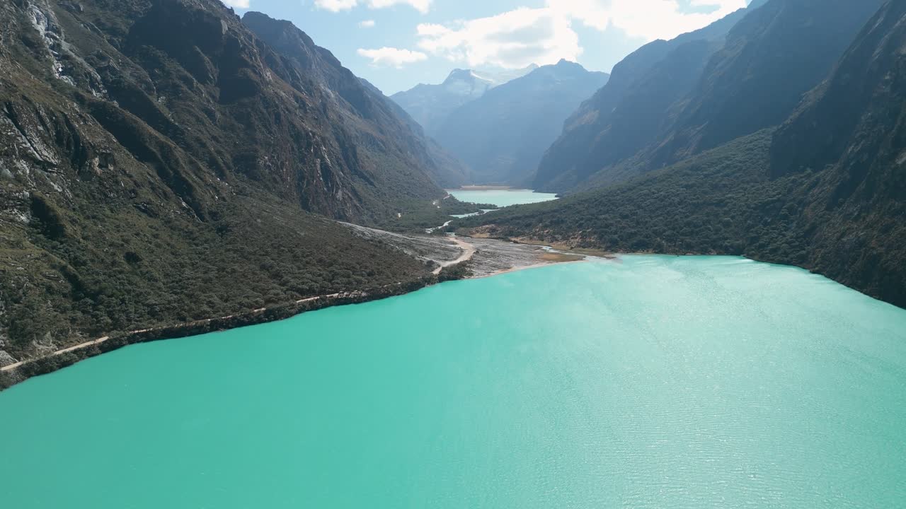 Aerial shot with a slow tilt up reveals the vivid turquoise waters of Lagunas de Llanganuco nestled in a dramatic Andean valley, surrounded by towering mountains in Peru