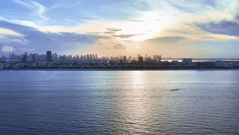 a drone flies toward miami beach from the atlantic ocean at sunset, capturing the sea, skyline, and shoreline, ending near the beach