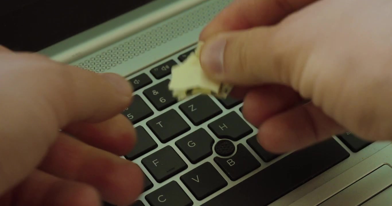 Close-up of hands tearing a paper note above a laptop keyboard, symbolizing password security, data protection, privacy, and avoiding unsafe password storage.
