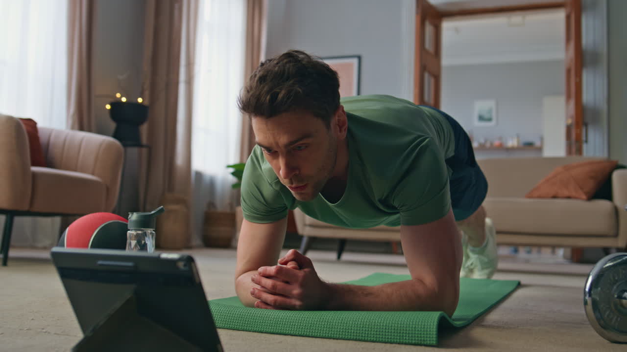 Athlete following online lesson standing plank position on yoga mat home.