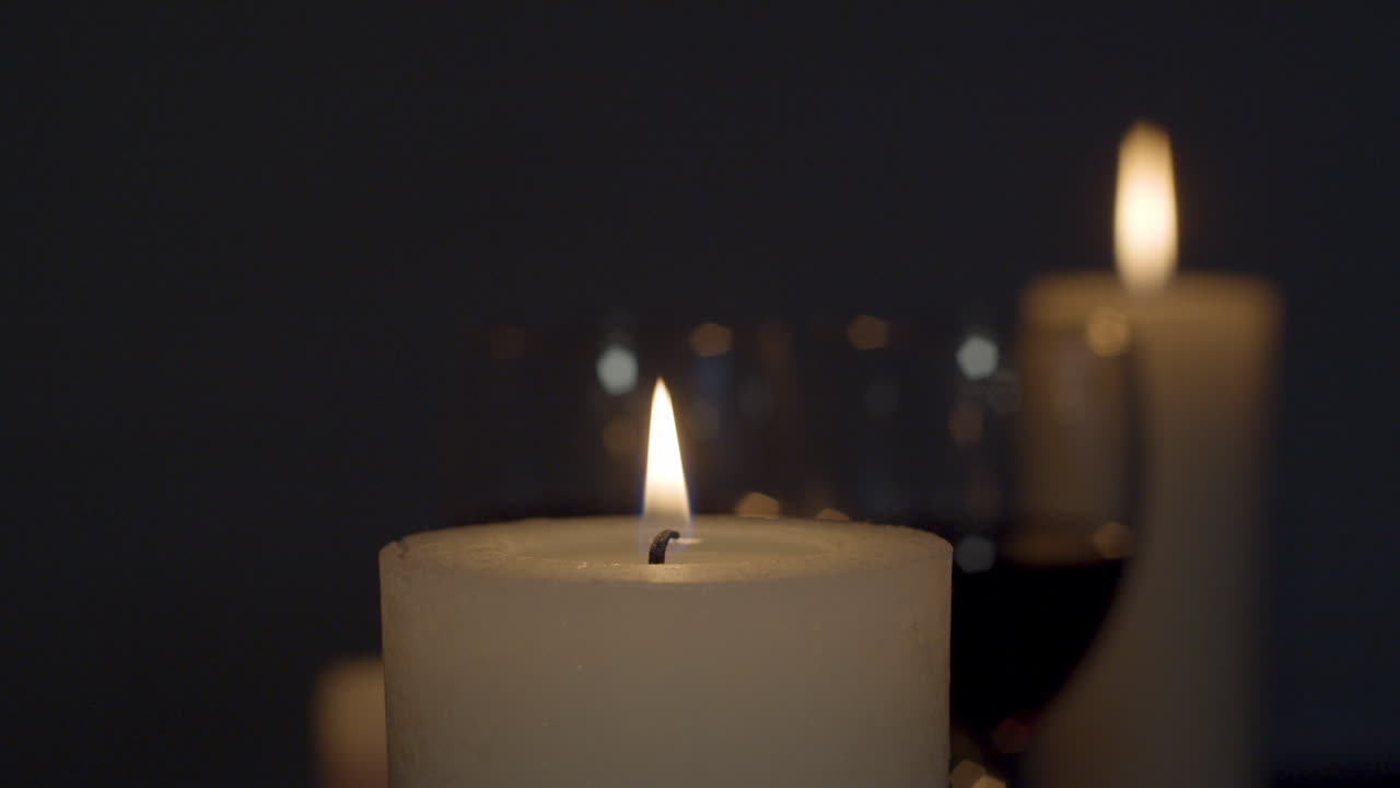 Candle being lit with match with a glass of wine and burning candle on background
