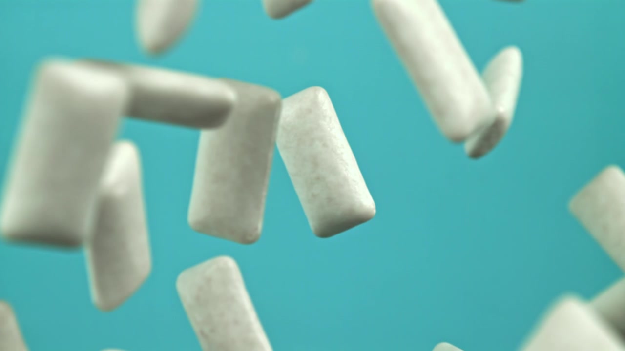 Pezzi di gomma da masticare bianca che cadono al rallentatore su sfondo blu.