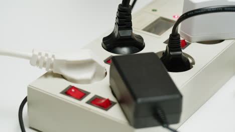 White power strip with many various of cords and cables in close-up. An extension cord with many power sockets. Adapter with phone, headphones, usb connectors.Tangled wires on table. Trying to untangle many messy cables.