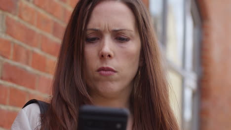 close up of stressed and worried woman outdoors with financial worries about cost of living crisis debt and paying bills looking at mobile phone on city street 1