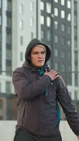 coach with clasped hand turning head and stretching arms in preparation for sports activity in modern urban sports arena surrounded by residential buildings