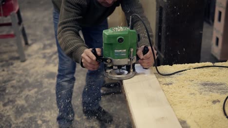 male carpenter worker in protective glasses grinds the wooden bar. craftsman polishing with manual grinding machine at wood workshop. front view