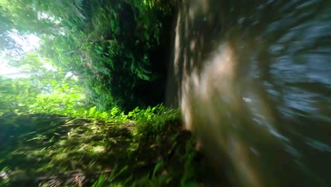 vertical fpv drone shot over fast streaming river through caves while a blond woman is enjoying the water falling from the waterfall