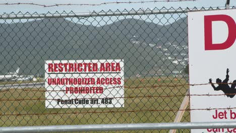 signs on airport perimeter with plane in bg