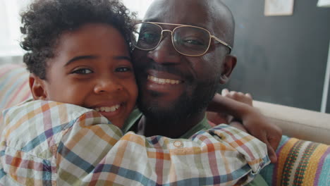 portrait of joyous african american father and little son hugging each other at home