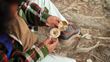 closeup shot of man sitting on tree root ground holding vintage compass in hand wearing flannel shirt and hiking boots during outdoor exploration in west virginia, america