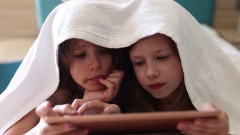 two girls under blanket using tablet