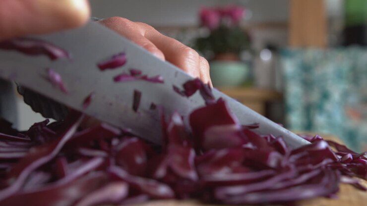 Primissimo piano della mano di una donna che taglia delicatamente a pezzi cavolo cappuccio viola italiano con un coltello affilato a punta arrotondata in cucina